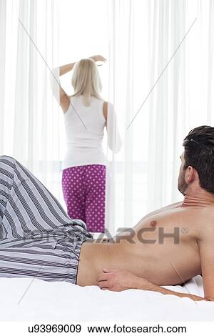 Young man looking at woman standing by window in hotel room View Large Photo Image Stock Photo - Young man looking at woman standing by window in hotel room. Fotosearch