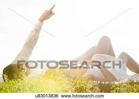 Young man lying with girlfriend while pointing against clear sky View Large Photo Image Stock Photograph - Young man lying with girlfriend while pointing against clear sky. Fotosearch