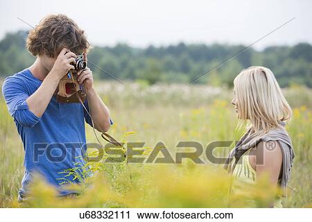 Stock Image - Young man photographing woman in field. Fotosearch
