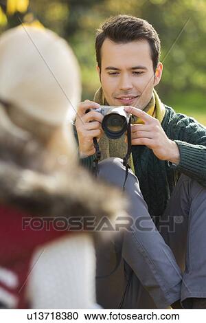 Stock Image - Young man photographing woman in park. Fotosearch
