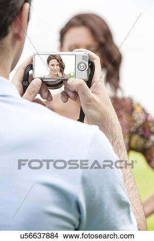 Young man photographing woman through digital camera in park View Large Photo Image Picture - Young man photographing woman through digital camera in park. Fotosearch