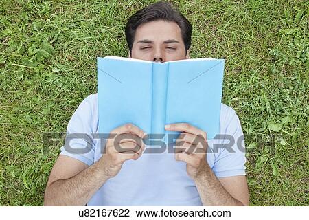 Young man reading book while lying on grass View Large Photo Image Stock Image - Young man reading book while lying on grass. Fotosearch