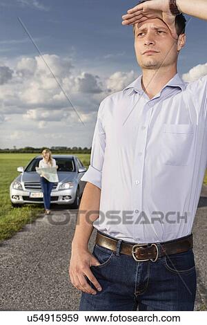 Young man shielding eyes with woman and car in background at countryside View Large Photo Image Stock Photo - Young man shielding eyes with woman and car in background at countryside. Fotosearch
