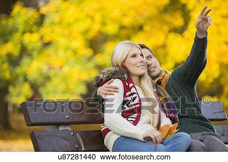 Stock Image - Young man showing something to woman while gesturing in park during autumn. Fotosearch