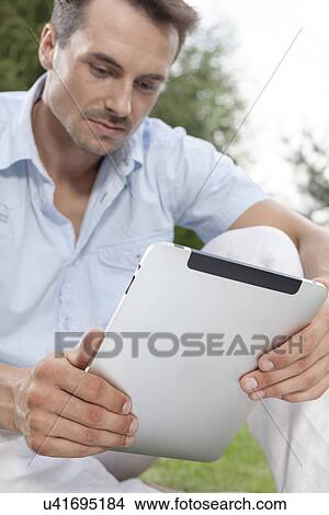 Picture - Young man using digital tablet in park. Fotosearch