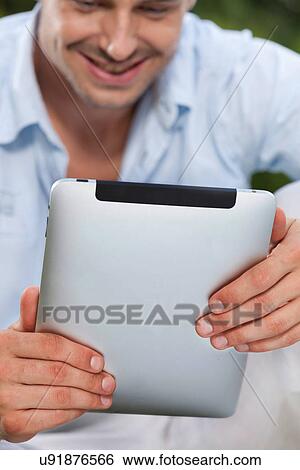 Stock Photograph - Young man using digital tablet in park. Fotosearch