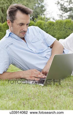 Young man using laptop in park View Large Photo Image Stock Image - Young man using laptop in park. Fotosearch