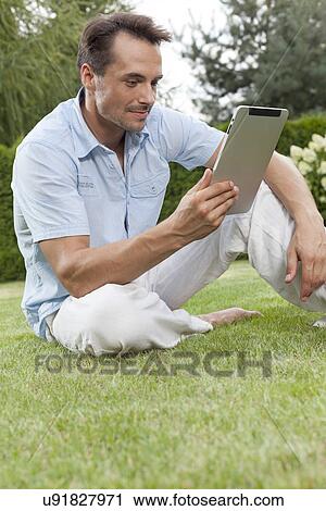 Stock Image - Young man using tablet computer in park. Fotosearch