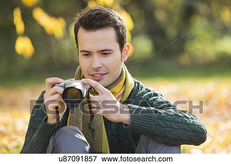Young man watching photographs on digital camera in park during autumn View Large Photo Image Stock Photo - Young man watching photographs on digital camera in park during autumn. Fotosearch