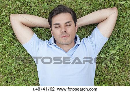 Young man with hands behind head lying on grass View Large Photo Image Stock Image - Young man with hands behind head lying on grass. Fotosearch