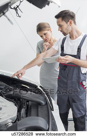 Stock Photo - Young repair worker explaining car engine to worried customer in workshop. Fotosearch