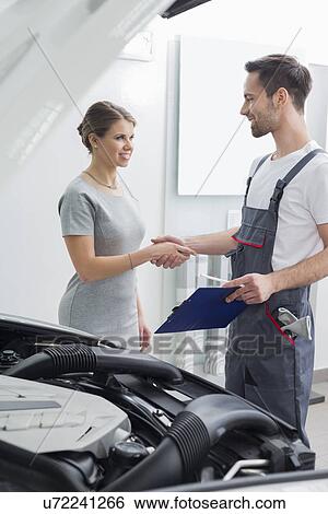 Stock Photograph - Young repair worker shaking hands with customer in car workshop. Fotosearch