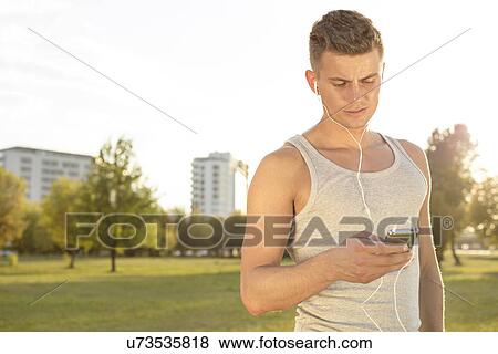 Young runner listening to music through cell phone in park View Large Photo Image Stock Photo - Young runner listening to music through cell phone in park. Fotosearch