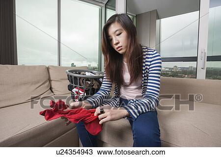 Stock Image - Young woman doing laundry work in living room at home. Fotosearch
