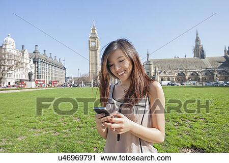 Stock Image - Young woman text messaging through smart phone against Big Ben at London, England, UK. Fotosearch