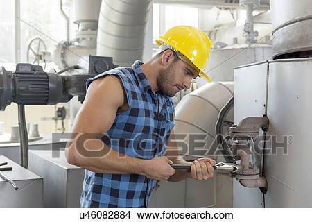 Picture - Young worker using wrench on industrial machine. Fotosearch