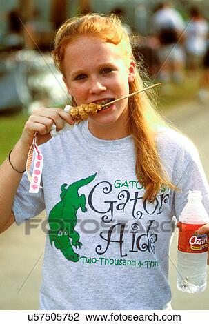Stock Image - A stock photo of a "Gator Aide" l enjoys some 'gator on a stick during a break at the Texas Gatorfest in Anhuac.. Fotosearch