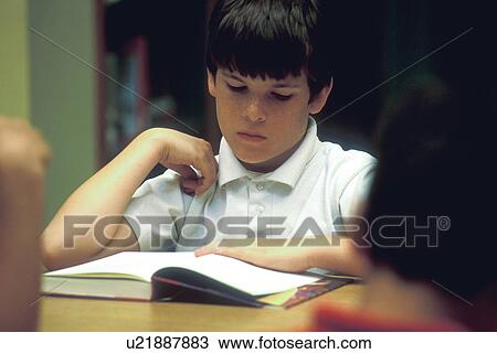 Stock Image - a young elementary student reading a textbook in class. Fotosearch