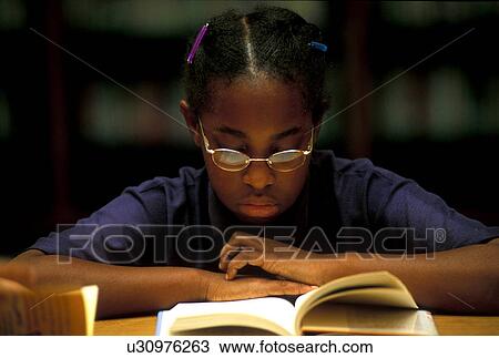 Stock Image - A young elementary student reading a book in the library. Fotosearch