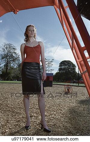 Stock Image - Woman in skirt standing under slide on playground. Fotosearch
