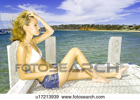 Stock Photo - Woman sitting on a pier . Fotosearch