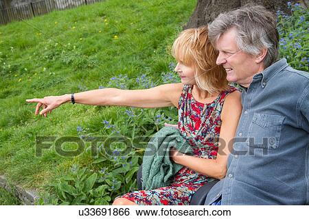 Adult couple sitting on bench in park View Large Photo Image Stock Photograph - Adult couple sitting on bench in park. Fotosearch