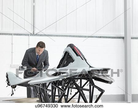 Stock Image - Automotive designer inspecting part-built supercar in car factory. Fotosearch