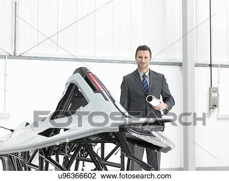 Stock Image - Automotive designer with part-built supercar in car factory, portrait. Fotosearch