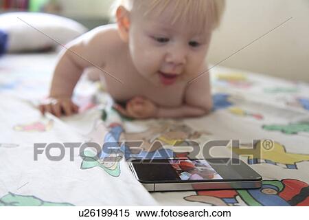 Stock Photography - Baby plays with smartphone on bed. Fotosearch