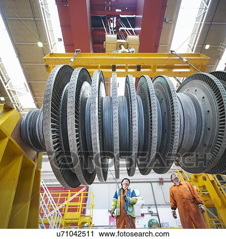 Stock Image - Banksman and crane operator lift turbine during power station outage, low angle view. Fotosearch