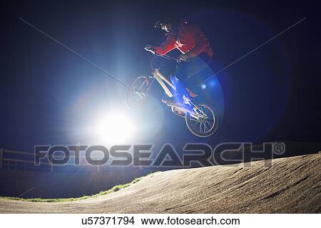 Picture - BMX-cyclist jumps his bike at night time. Fotosearch