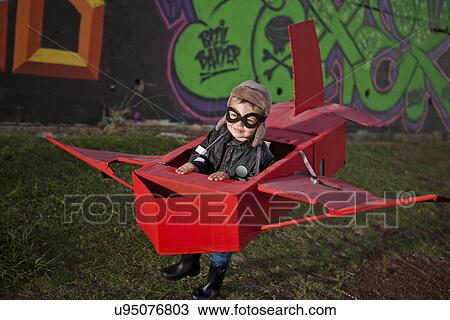 Stock Image - Boy wearing flying goggles running in toy airplane in park at night. Fotosearch