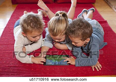 Stock Photograph - Boys and a girl using digital tablet at nursery school. Fotosearch