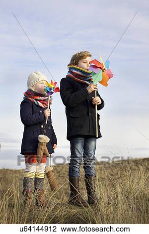 Stock Image - Brother and sister blowing on paper windmills at coast. Fotosearch