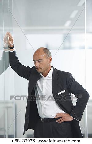 Businessman contemplating against reflective wall View Large Photo Image Stock Photograph - Businessman contemplating against reflective wall. Fotosearch