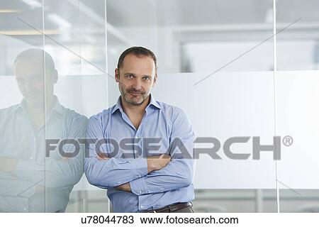 Stock Image - Businessman leaning against reflective wall. Fotosearch
