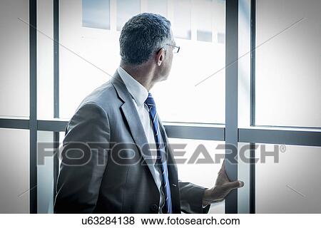 Stock Photo - Businessman looking out through glass wall. Fotosearch