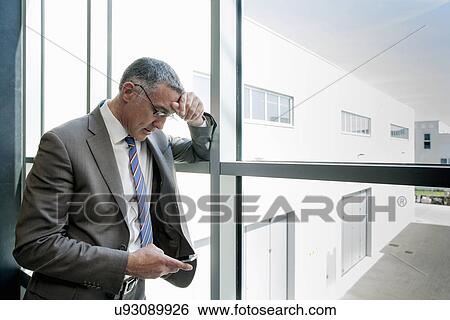 Stock Photograph - Businessman using smartphone by glass wall. Fotosearch