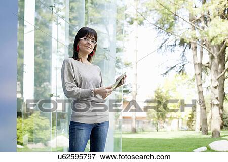 Businesswoman holding digital tablet by glass wall View Large Photo Image Stock Photo - Businesswoman holding digital tablet by glass wall. Fotosearch
