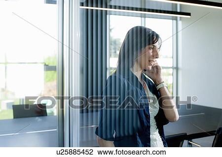 Stock Image - Businesswoman on smartphone behind glass wall. Fotosearch