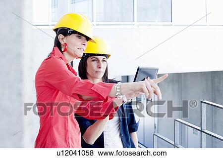 Stock Photo - Businesswomen in safety helmet taking photograph. Fotosearch