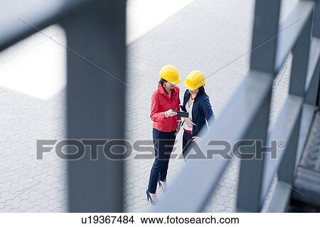 Picture - Businesswomen in safety helmet using digital tablet. Fotosearch