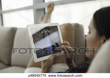 Stock Photography - Close up of young woman on sofa using digital tablet. Fotosearch