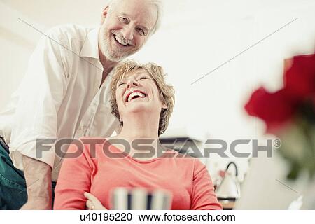 Stock Image - Couple laughing in kitchen, portrait. Fotosearch