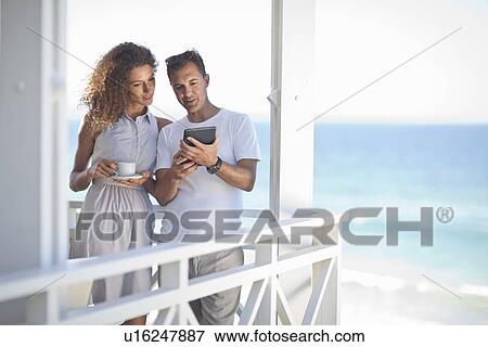 Couple looking at digital tablet on beach house balcony View Large Photo Image Stock Photo - Couple looking at digital tablet on beach house balcony. Fotosearch
