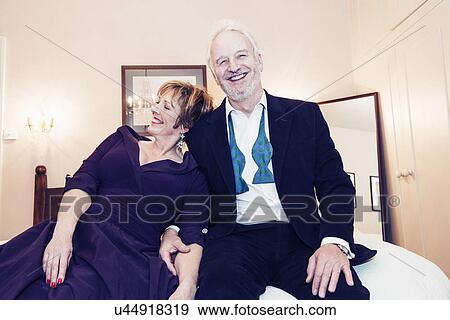 Stock Photo - Couple sitting on bed, laughing. Fotosearch