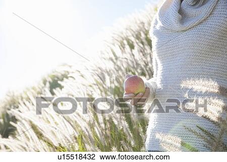 Stock Image - Cropped shot of young woman holding an apple in long grass. Fotosearch