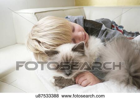 Stock Photo - Cute three year old boy with eyes closed hugging cat on sofa. Fotosearch