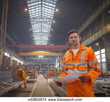 Engineer holding plans in marine fabrication factory, portrait View Large Photo Image Picture - Engineer holding plans in marine fabrication factory, portrait. Fotosearch