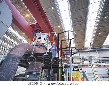 Picture - Engineer inspecting valves during power station outage, low angle view. Fotosearch